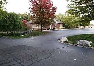 a_brick_house_is_surrounded_by_trees_and_a_driveway