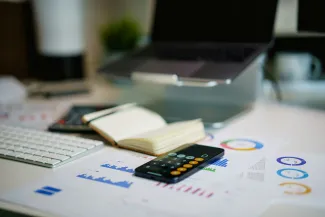 office desk with smartphone and financial charts by Jakub Żerdzicki courtesy of Unsplash.