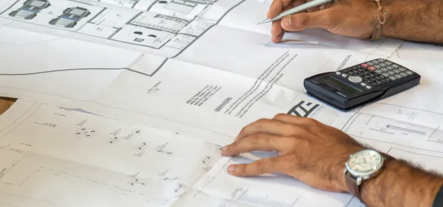 people reviewing architectural blueprints on desk by Pedro Miranda courtesy of Unsplash.