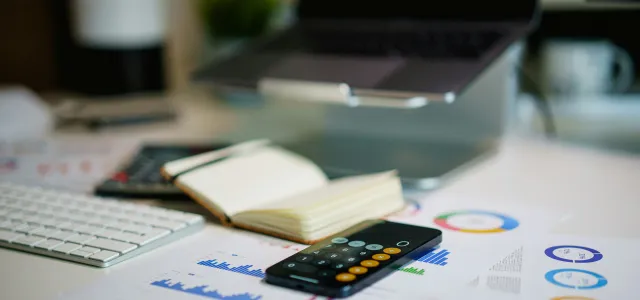 office desk with smartphone and financial charts by Jakub Żerdzicki courtesy of Unsplash.